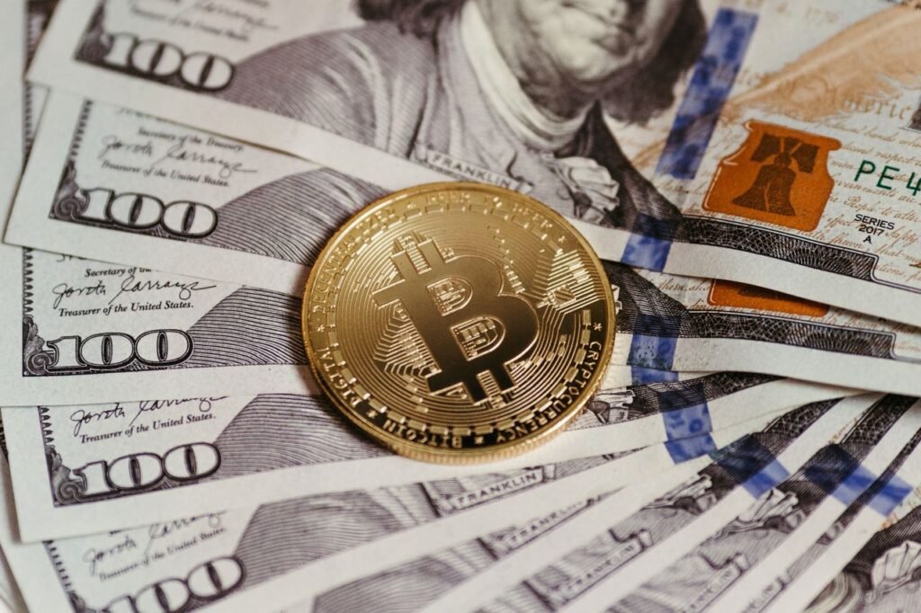 Exploring the Ripple Effects of the US Election on Cryptocurrency, Real Estate, Tesla, and Society Gold Bitcoin coin resting on US dollar bills showcasing digital and traditional currency.