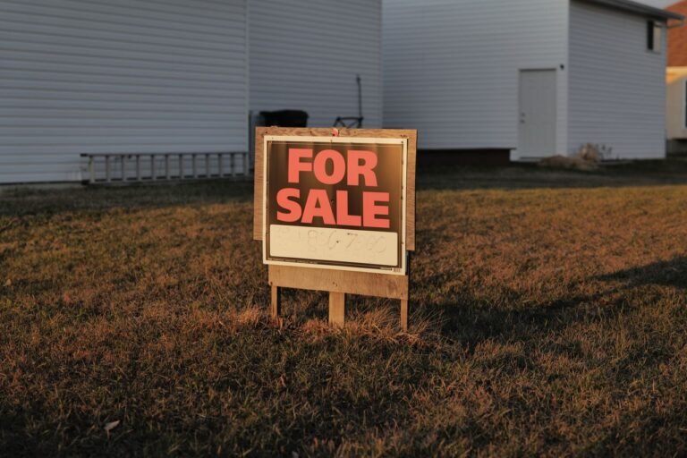 Close-up of a 'For Sale' sign in a suburban yard, indicating a property for sale.