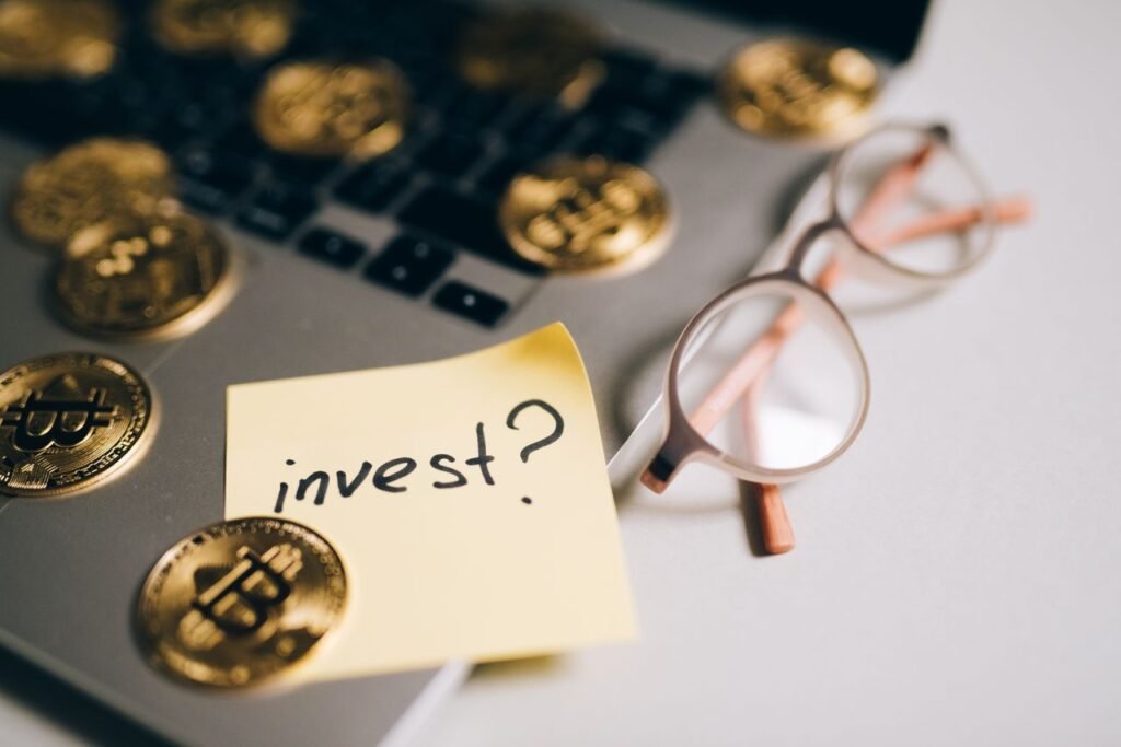 How Interest Rates Shape Real Estate Investing: What Buyers, Lenders, and Developers Need to Know A close-up of bitcoin coins on a laptop with eyeglasses and a sticky note reading 'invest?'