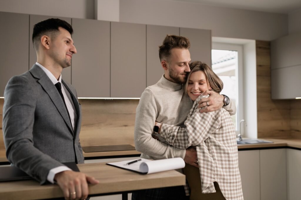 Before Your Homeowners Policy Renews, Check These 4 Things Happy couple embracing in their new home with a real estate agent present.